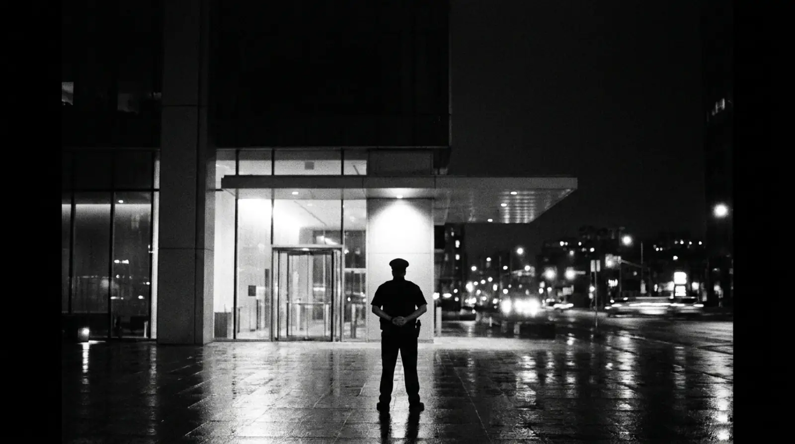 Agent de sécurité de dos, la nuit, devant l'entrée d'un immeuble